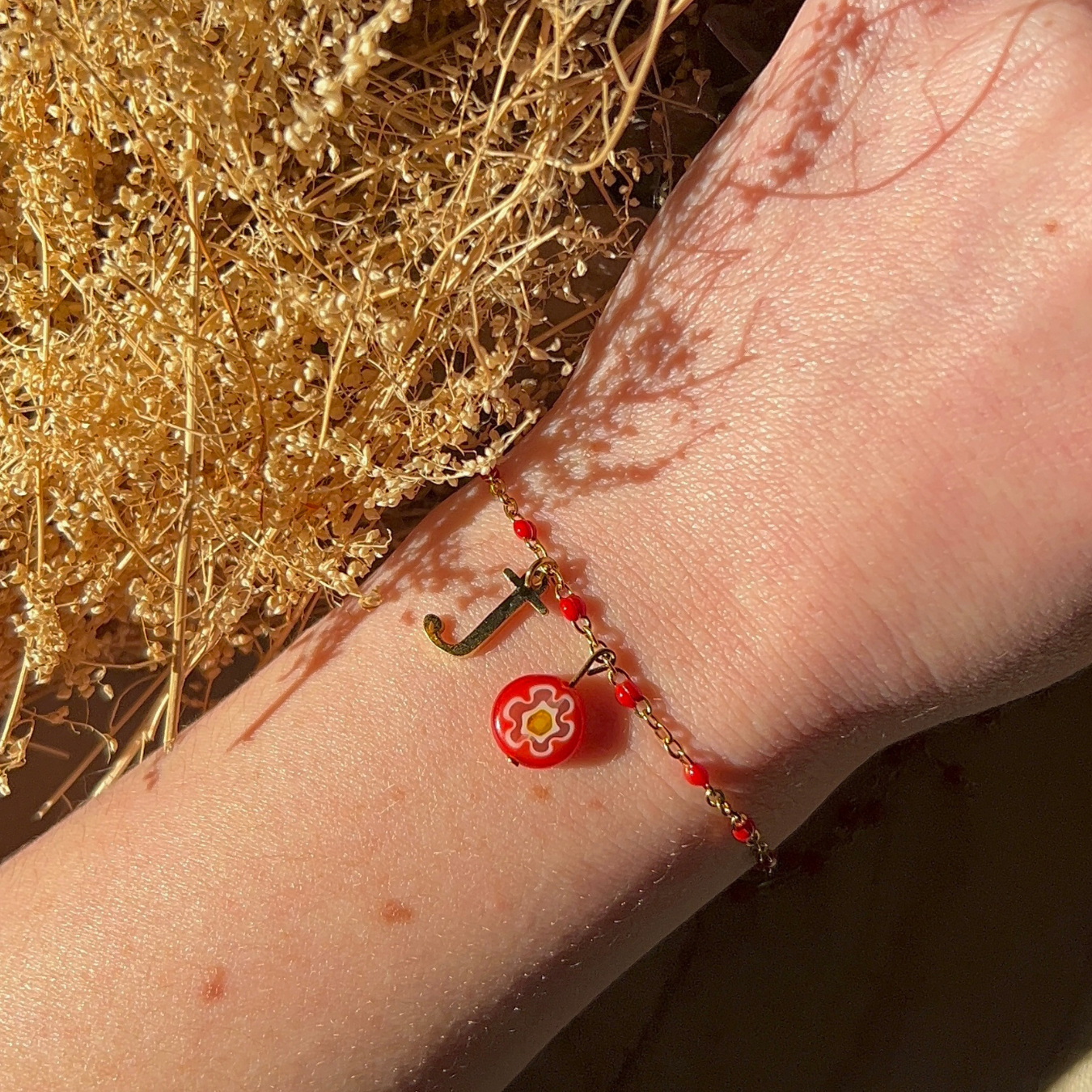 bracelet julie doré personnalisable avec lettre et perle Millefiori, présenté ici avec la lettre J et perle rouge