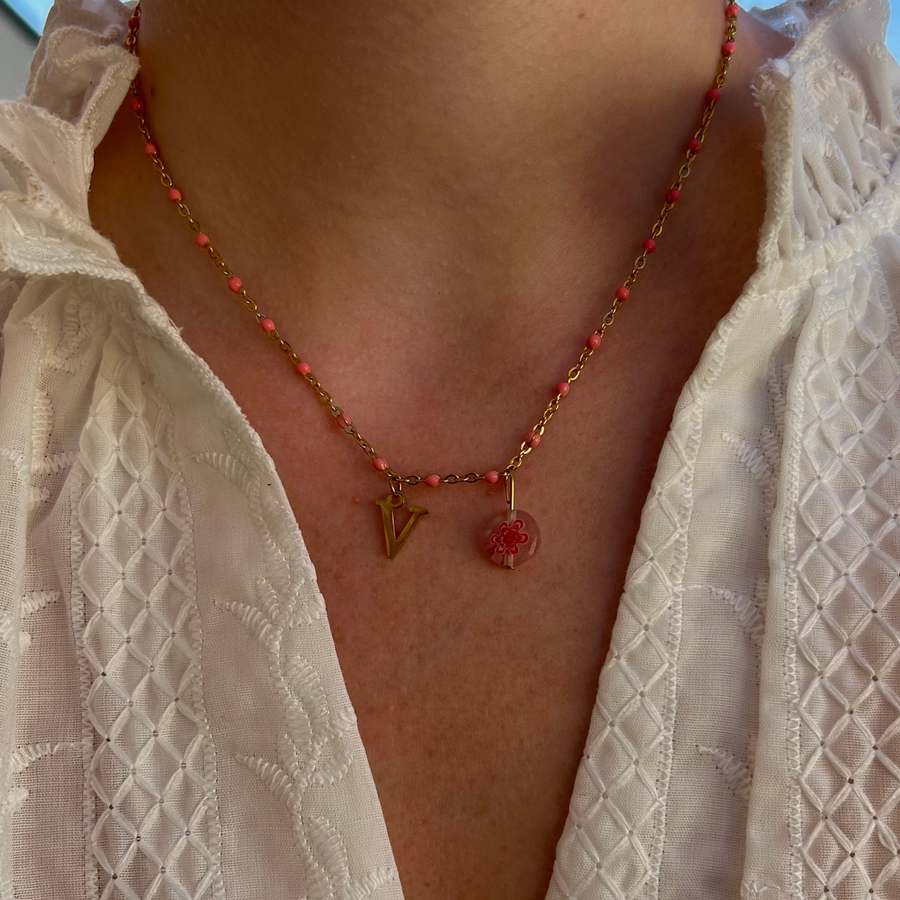 collier barbie doré personnalisable avec lettre et perle Millefiori, présenté ici avec la lettre V et perle rose 